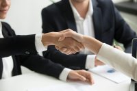 Men and women in suits shake hands during business transaction.